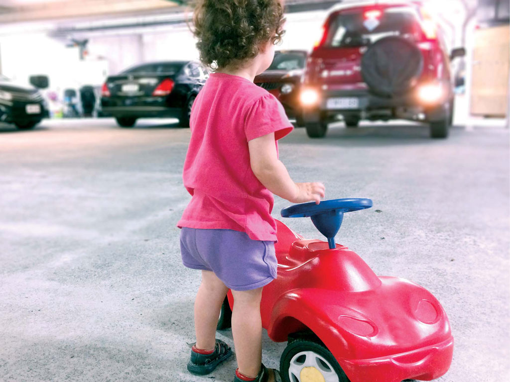 toddler at risk for accident by playing in a busy parking lot