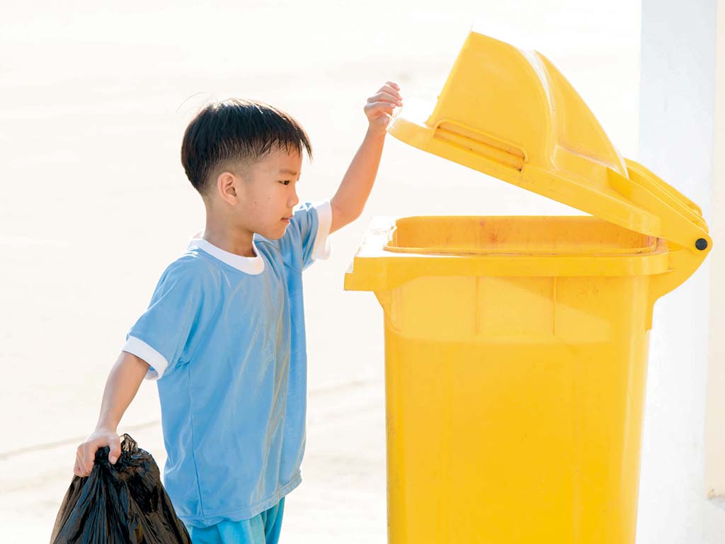 young boy about to place a trash bad in the trash bin