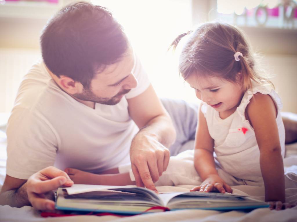 a dad and daughter lying down and reading a book together