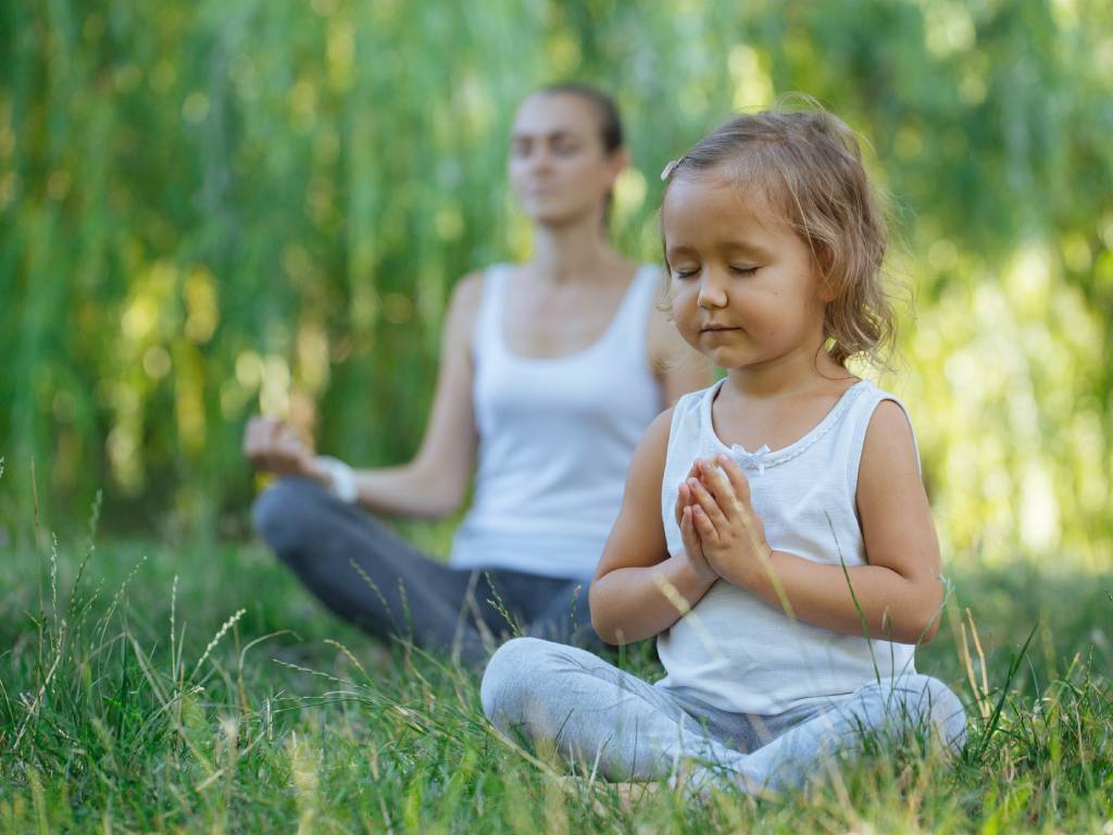 a mom and daughter practicing yoga outdoors
