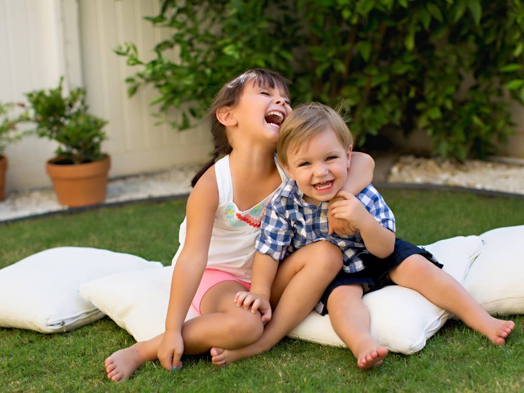 a young girl with her arm around a young boy laughing and smiling