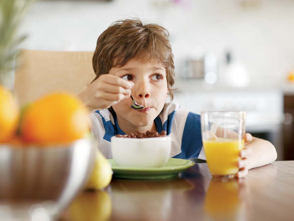 young boy eating cereal and drinking orange juice