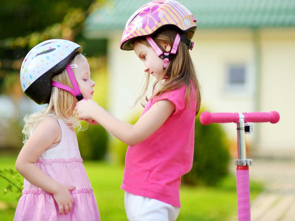 a girl securing a bike helmet on her younger sister