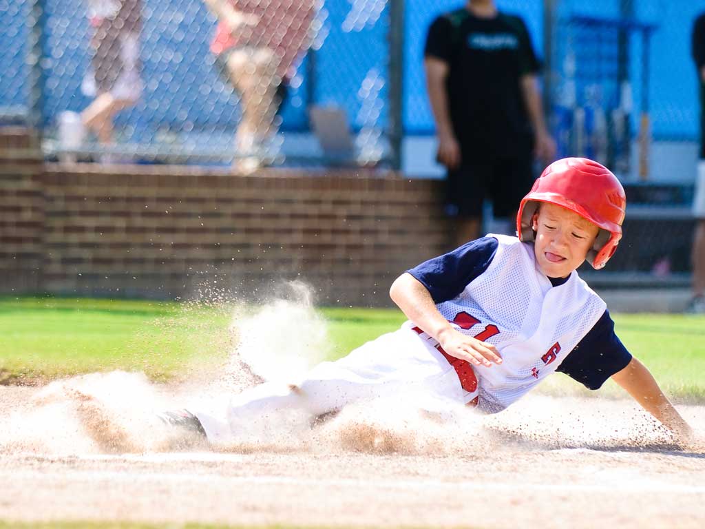 a young boy wearing a mouthguard playing baseball as he is sliding onto a base