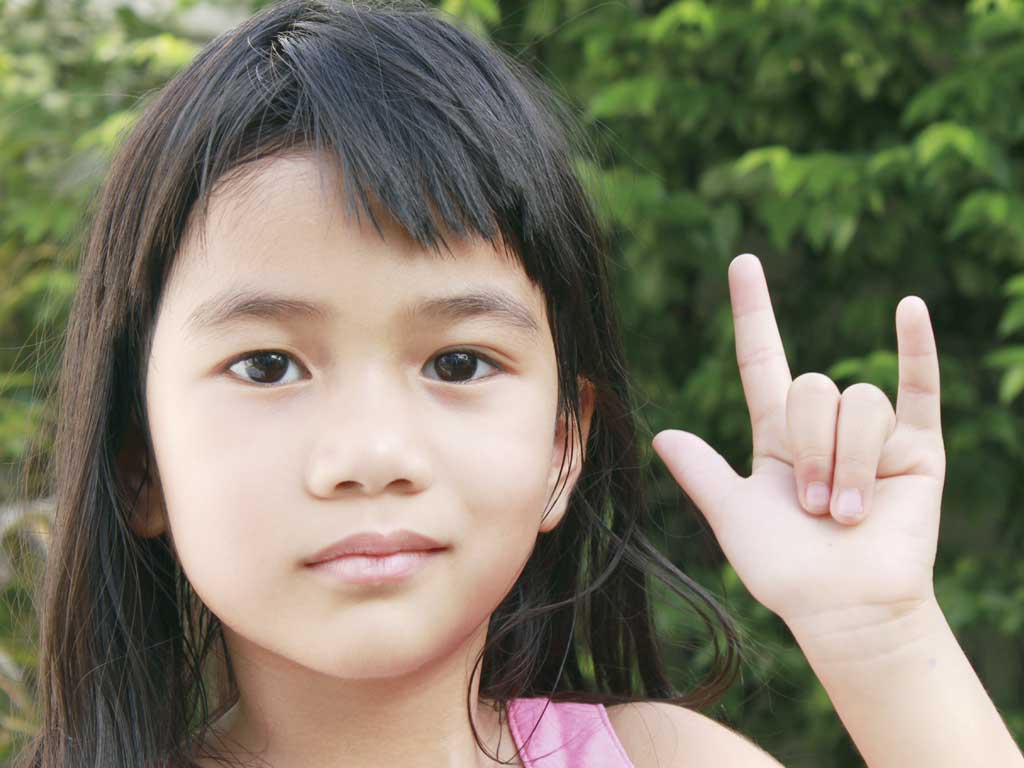 Young girl signing "I love you" in ASL.