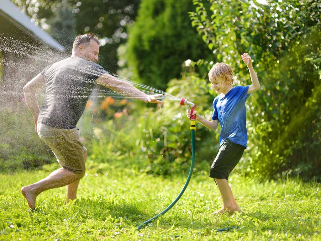 father and son playing with water hose