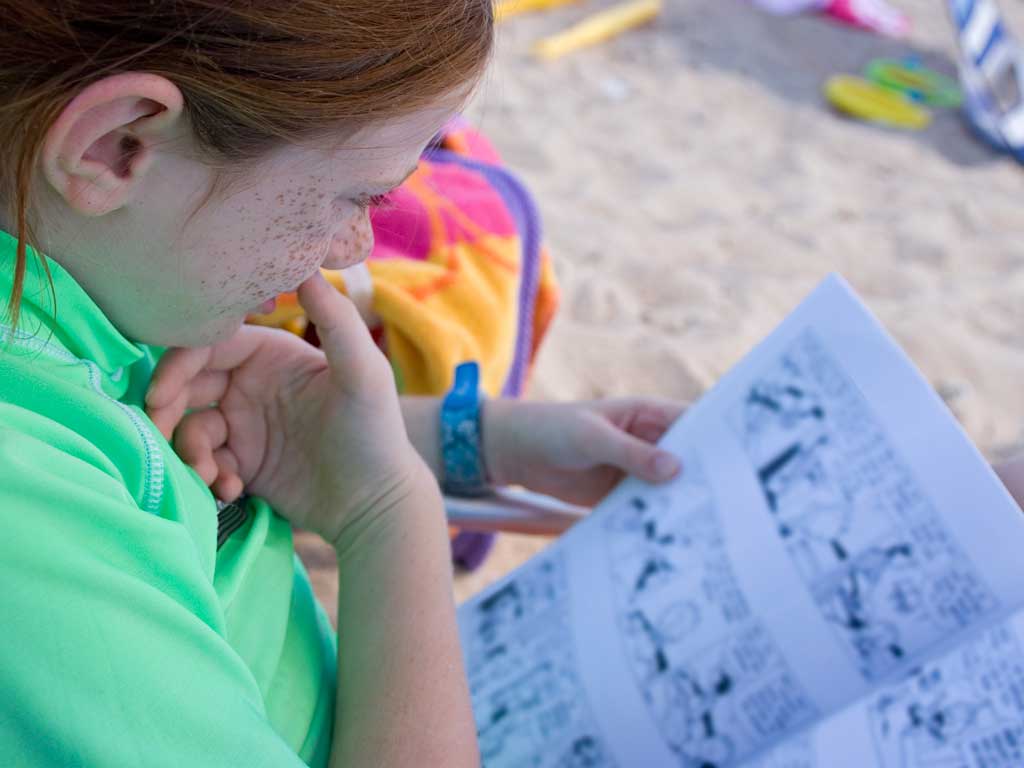 young girl reading a graphic novel at the beach