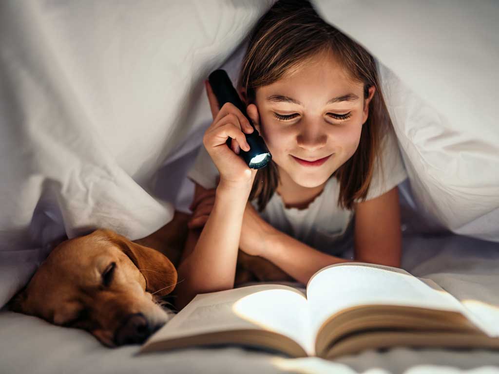 young girl reading under the blanket with her dog