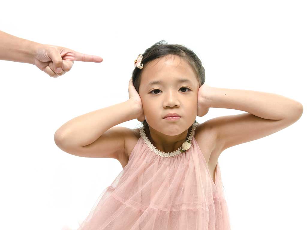 young girl holding hands to her ears while being scolded