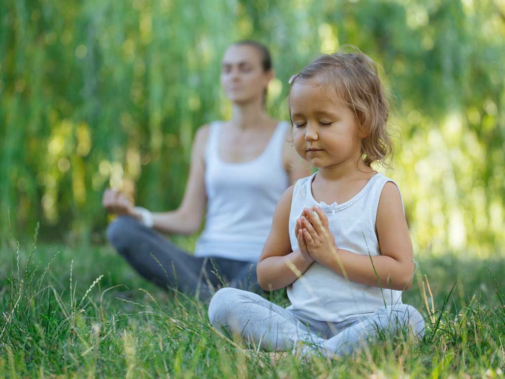 mother and daughter meditating outside