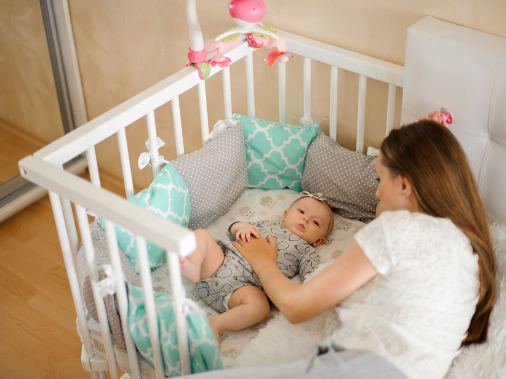 mom putting down baby in crib