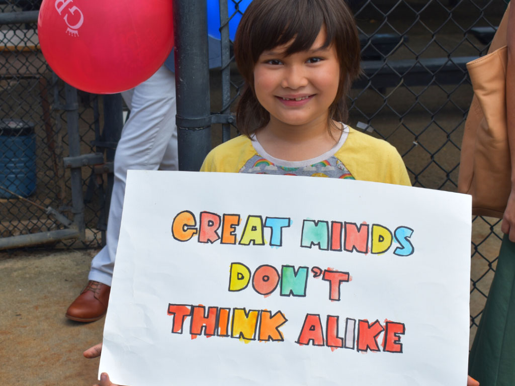 young child holding sign that says "Great Minds Don't Think Alike"