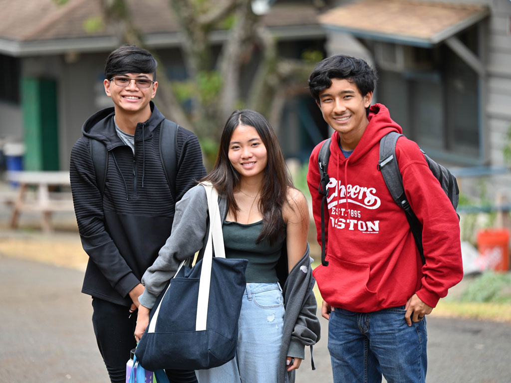 three teenage students smiling on campus