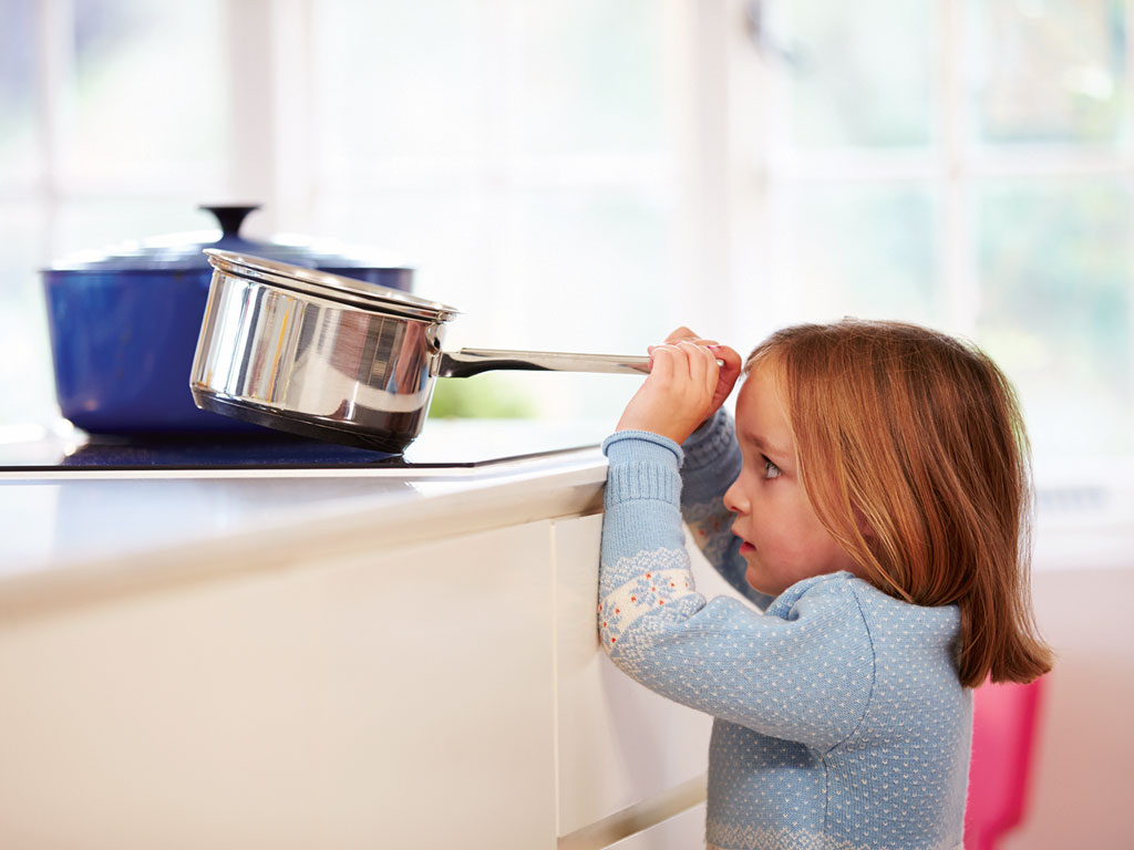 young girl touching pot on the stove