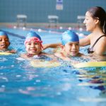 instructor teaching three kids how to swim