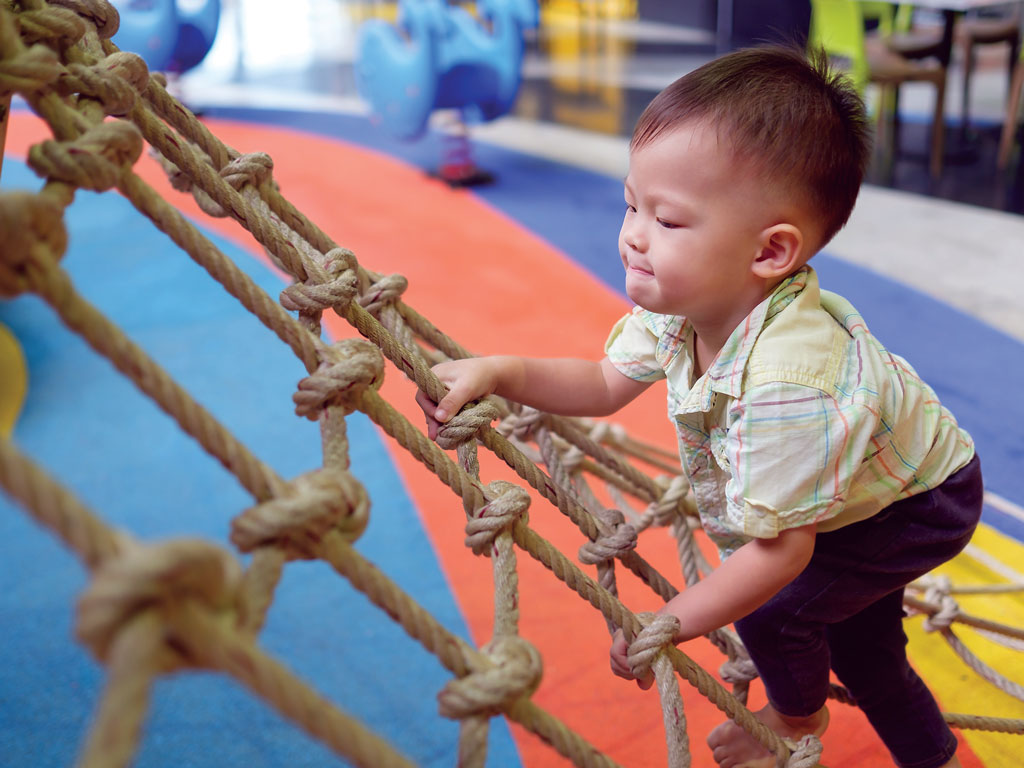 toddler boy climbing up a rope ladder