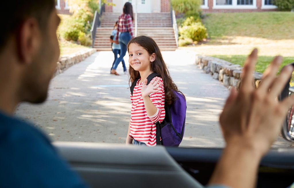 girl waving to parent as she enters middle school
