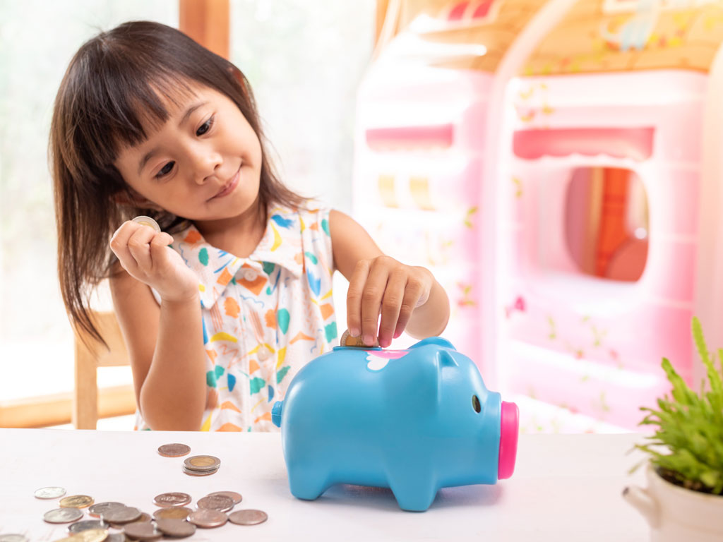 little girl putting money into her piggy bank