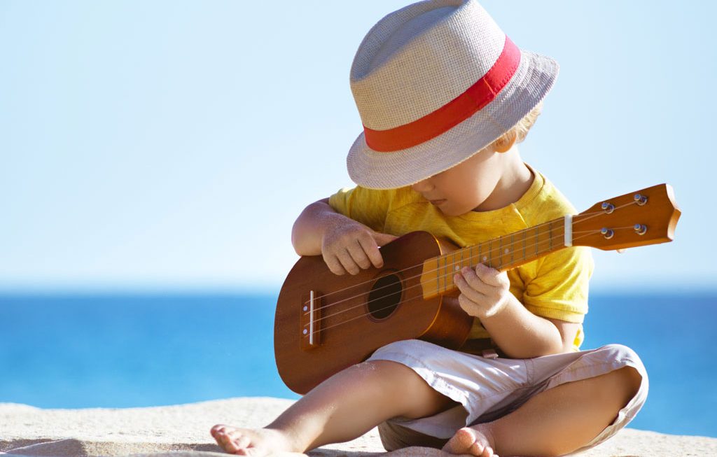 young boy playing the ukulele on the beach