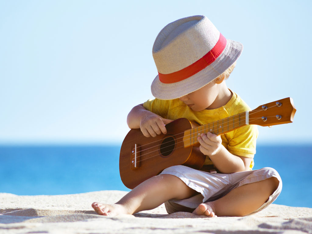 young boy playing the ukulele on the beach