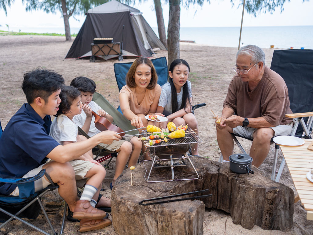 a family of six having a barbeque while camping near the beach