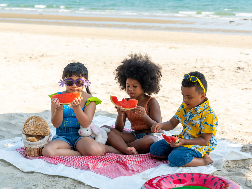 three kids eating watermelon on the beach
