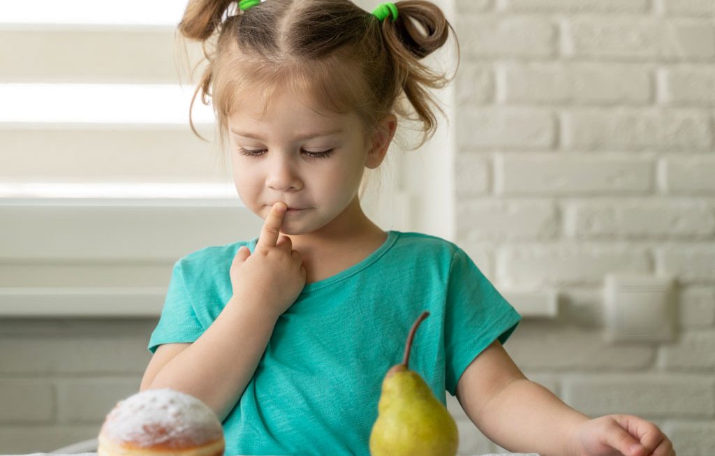 young girl trying to decide between a donut and a pear