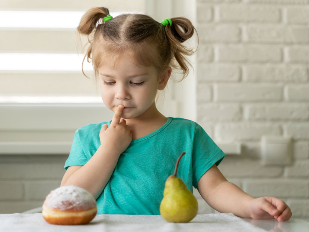 young girl trying to decide between a donut and a pear