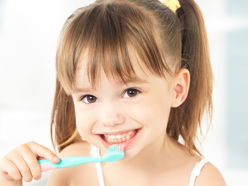 little girl smiling while brushing her teeth