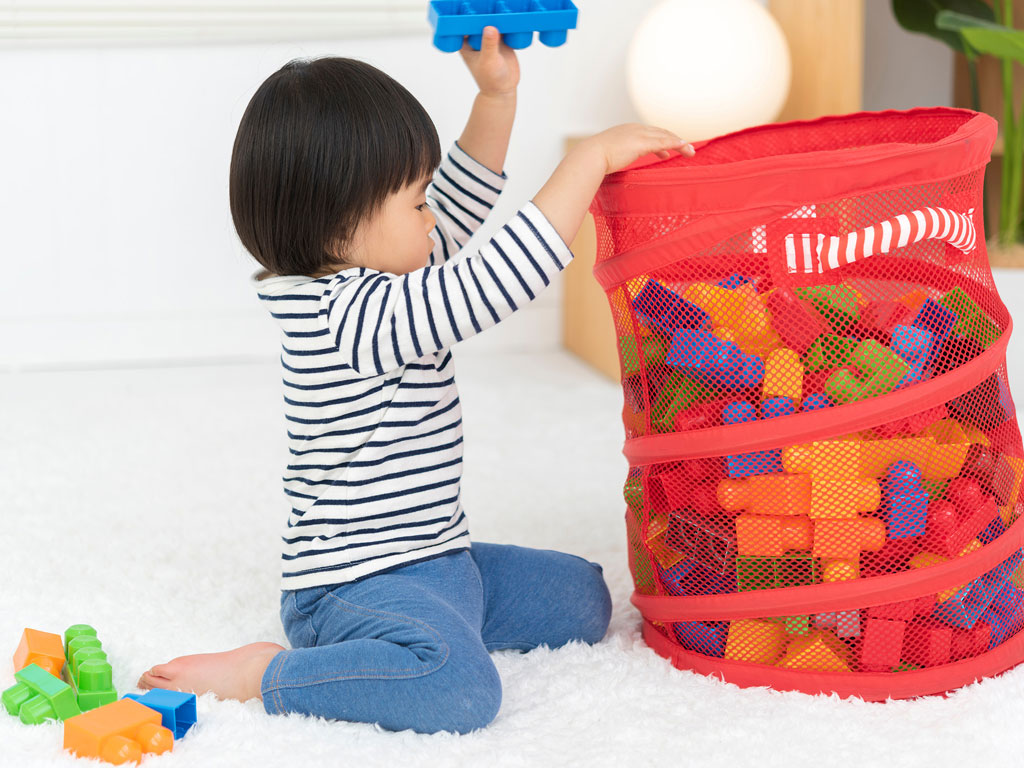 a young child putting away his toys in a bin