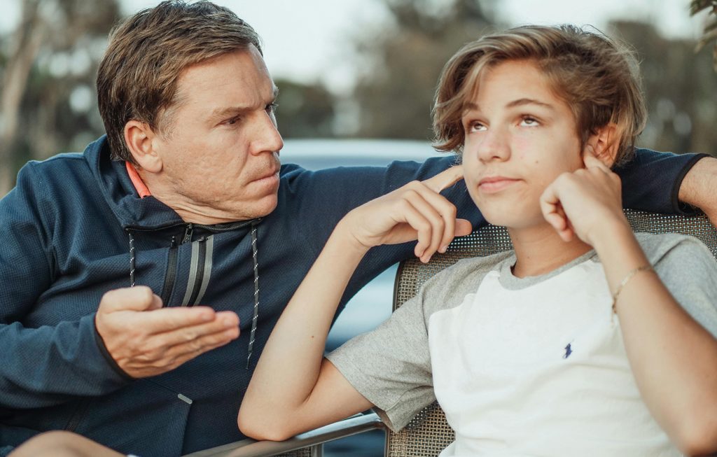teenage son with fingers in his ears as he's being scolded by his dad