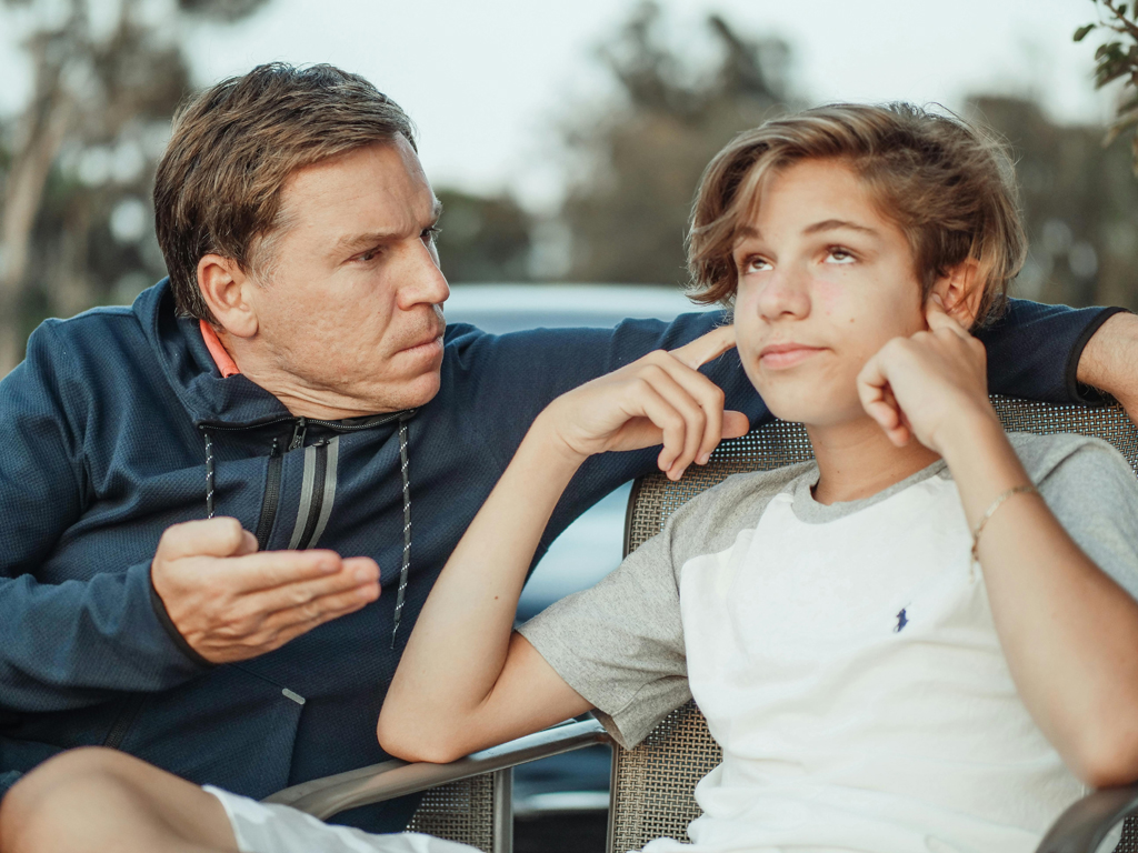teenage son with fingers in his ears as he's being scolded by his dad