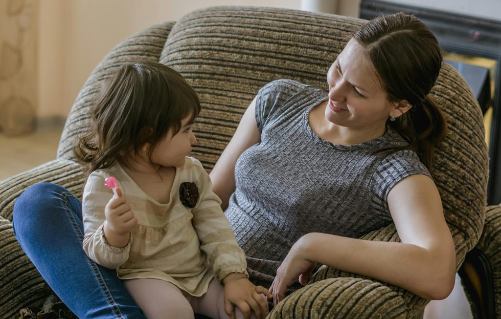 toddler holding lollipop while sitting on her mother's lap