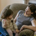 toddler holding lollipop while sitting on her mother's lap