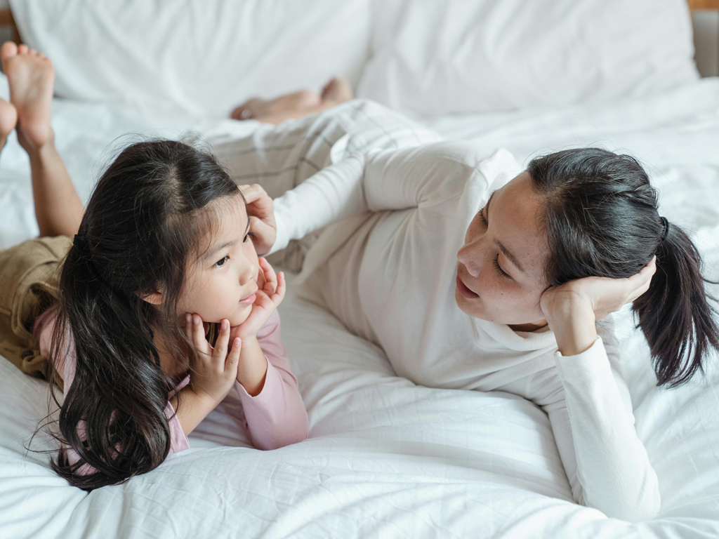 mom and daughter lying on a bed having a discussion