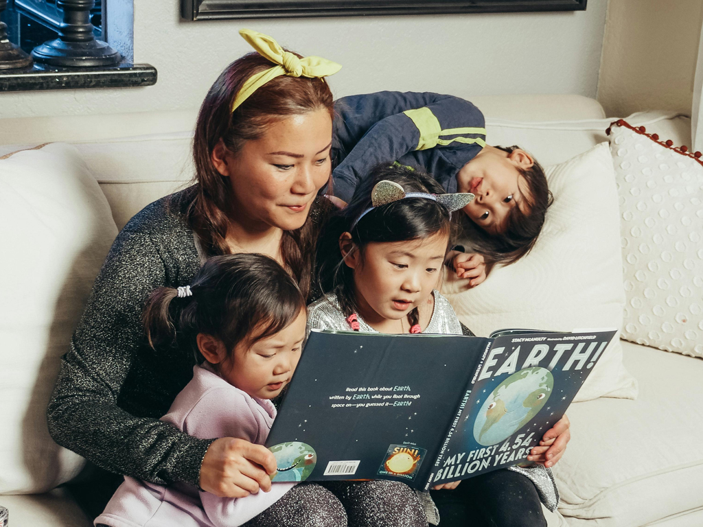 mom reading a story to her three children on the sofa