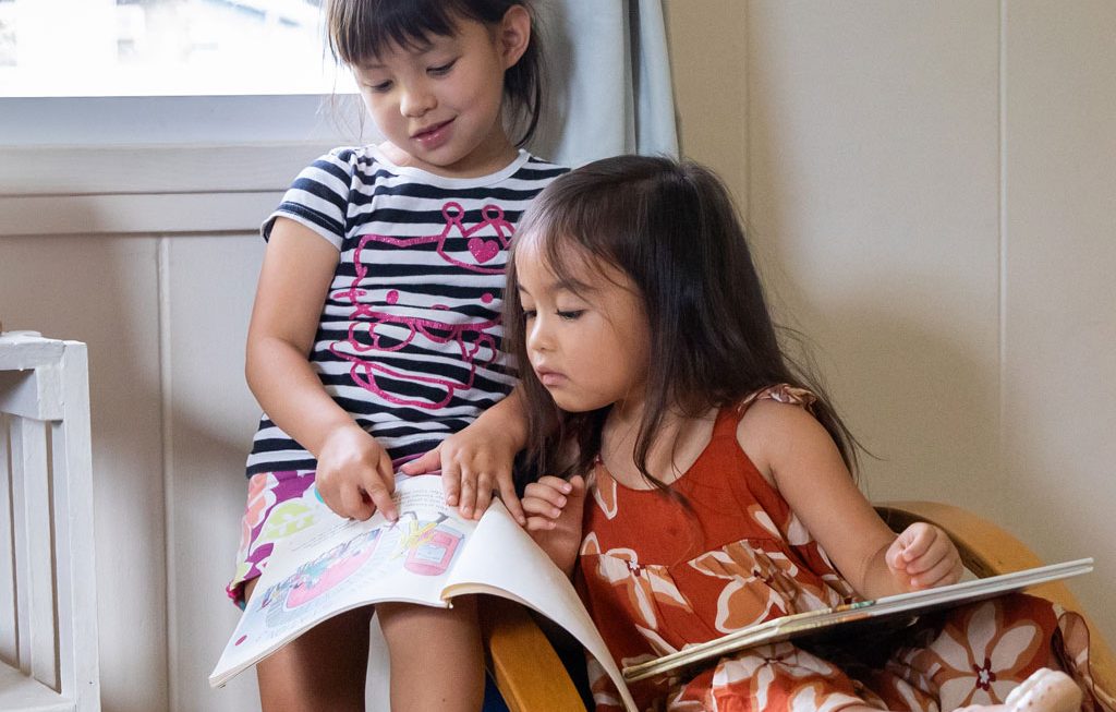 two girls sharing a chair and learning how to read