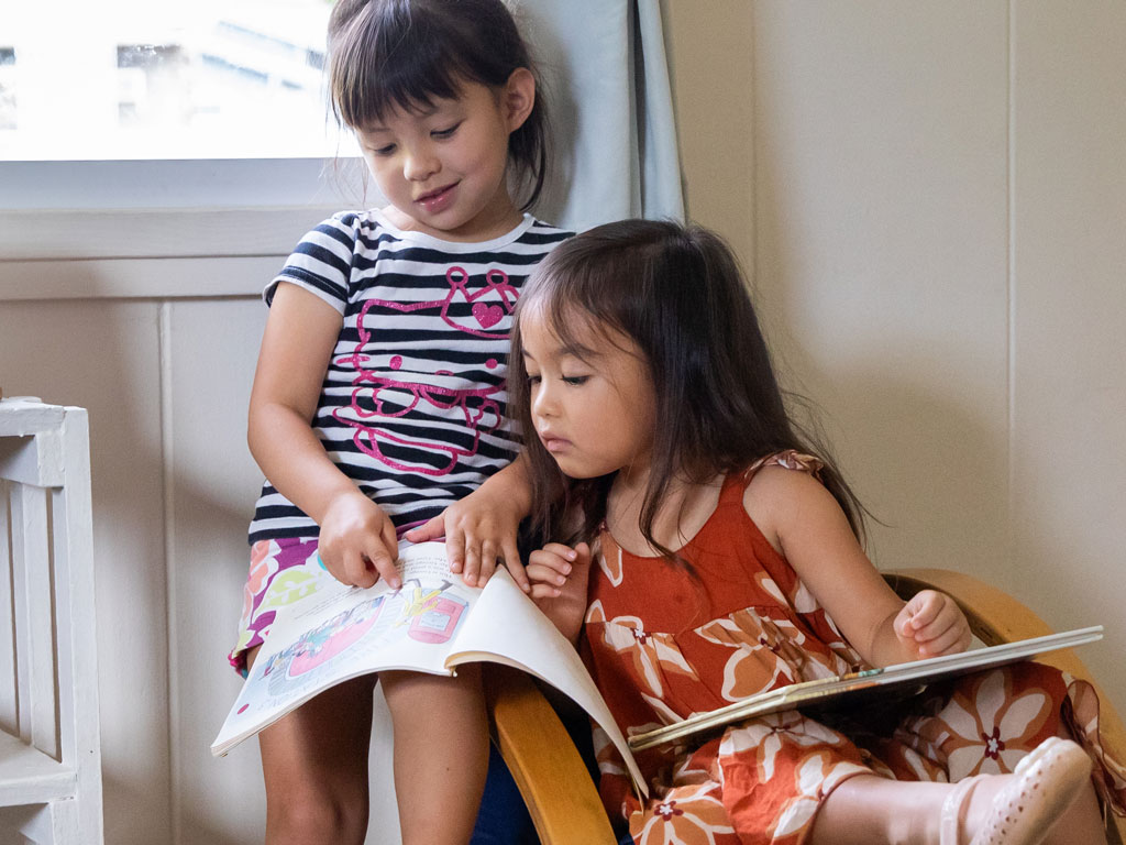 two girls sharing a chair and learning how to read