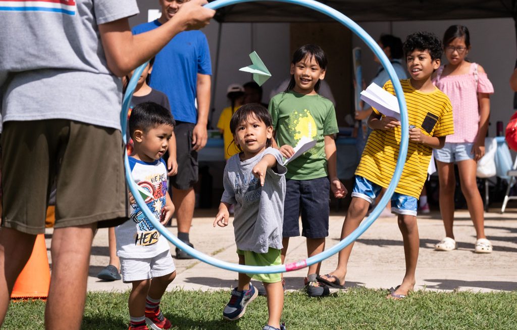 child throwing paper airplane through hula hoop at Leeward Discovery Fair