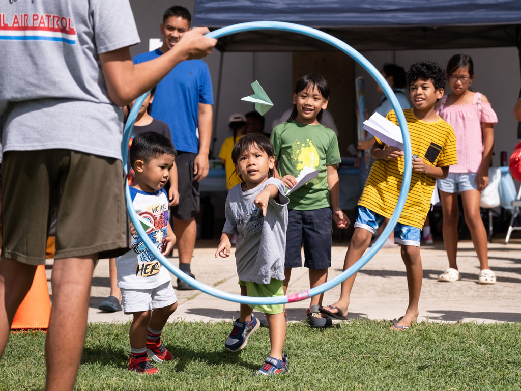 child throwing paper airplane through hula hoop at Leeward Discovery Fair