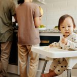 infant sitting in a high chair while parents are cooking