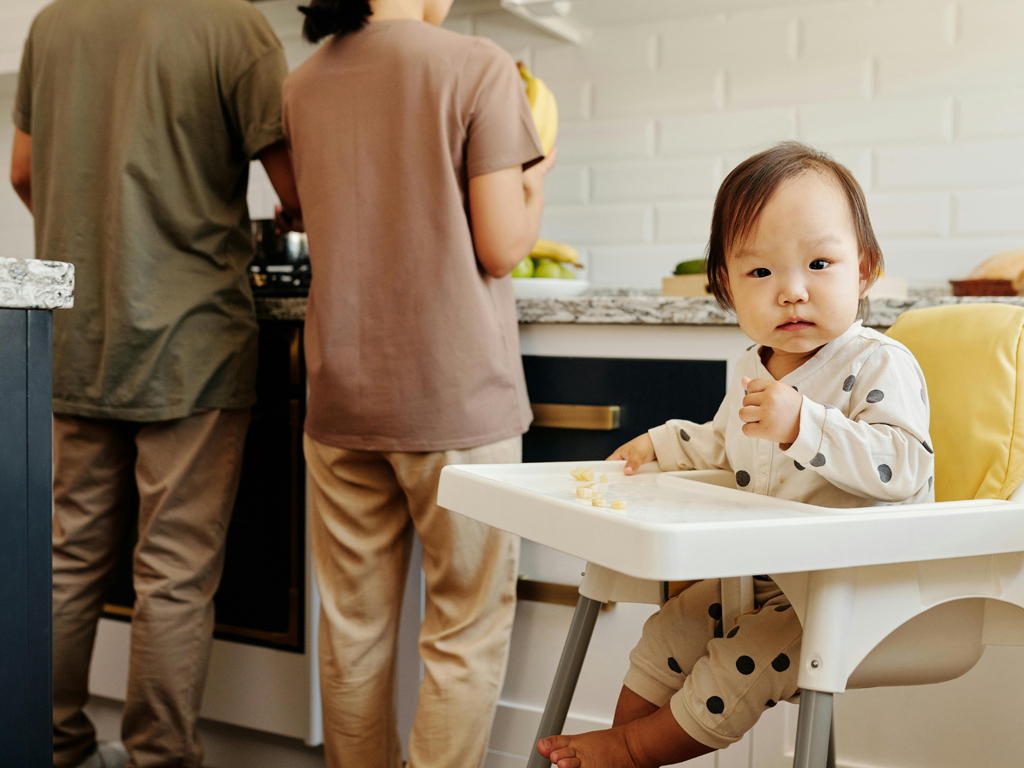 infant sitting in a high chair while parents are cooking