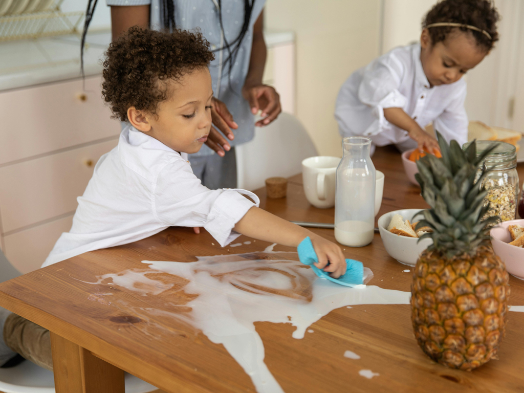 kids cleaning up the dining table after spilling milk