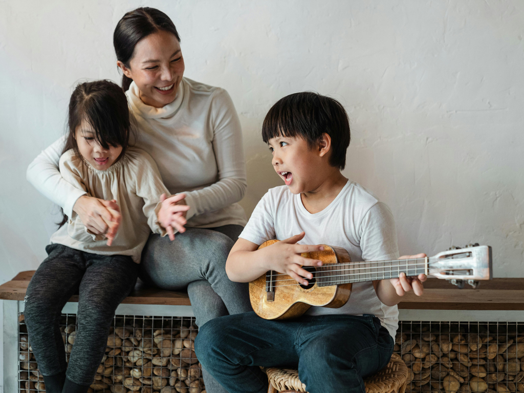 mom holding her daughter while watching her son play the ukulele