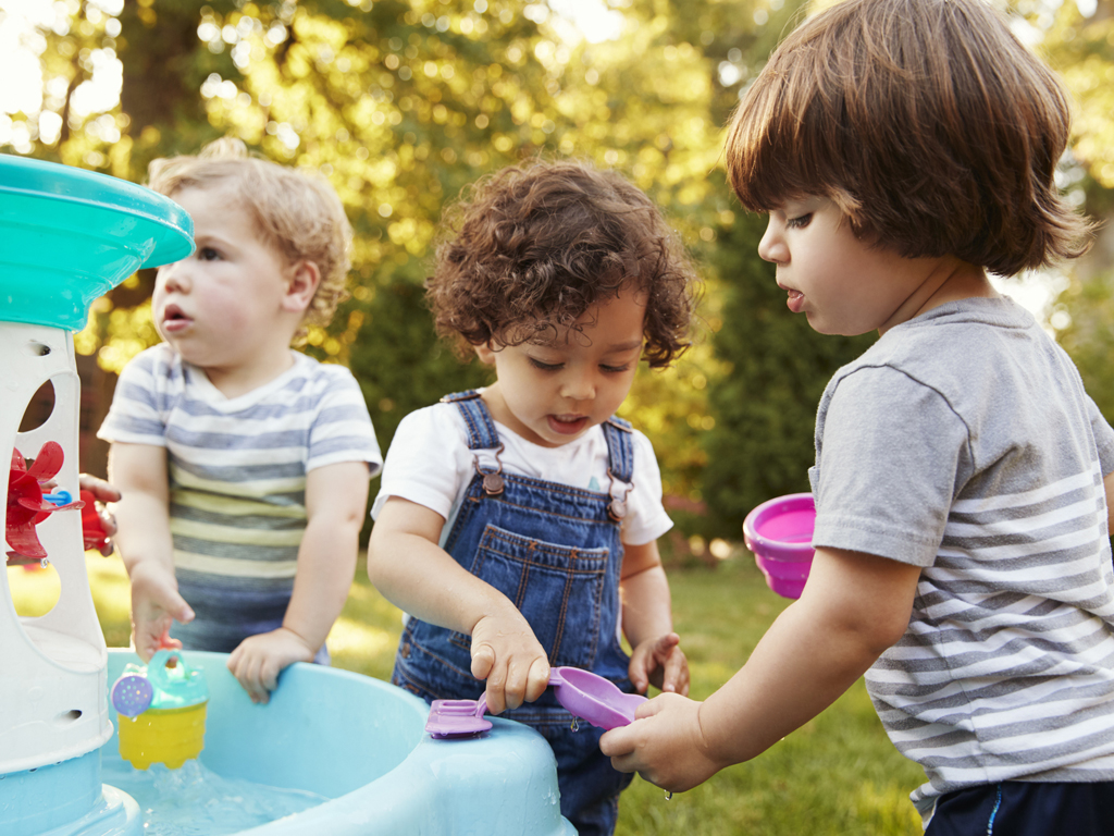 Group Of Young Children Playing With Water Table In Garden