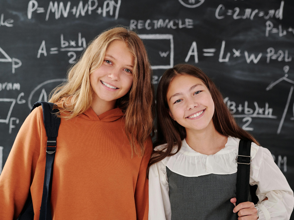 two high school age females smiling in front of a chalkboard