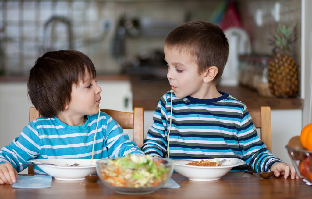 Two sweet children, boy brothers, having for lunch spaghetti at home, enjoying tasty food