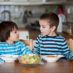 Two sweet children, boy brothers, having for lunch spaghetti at home, enjoying tasty food