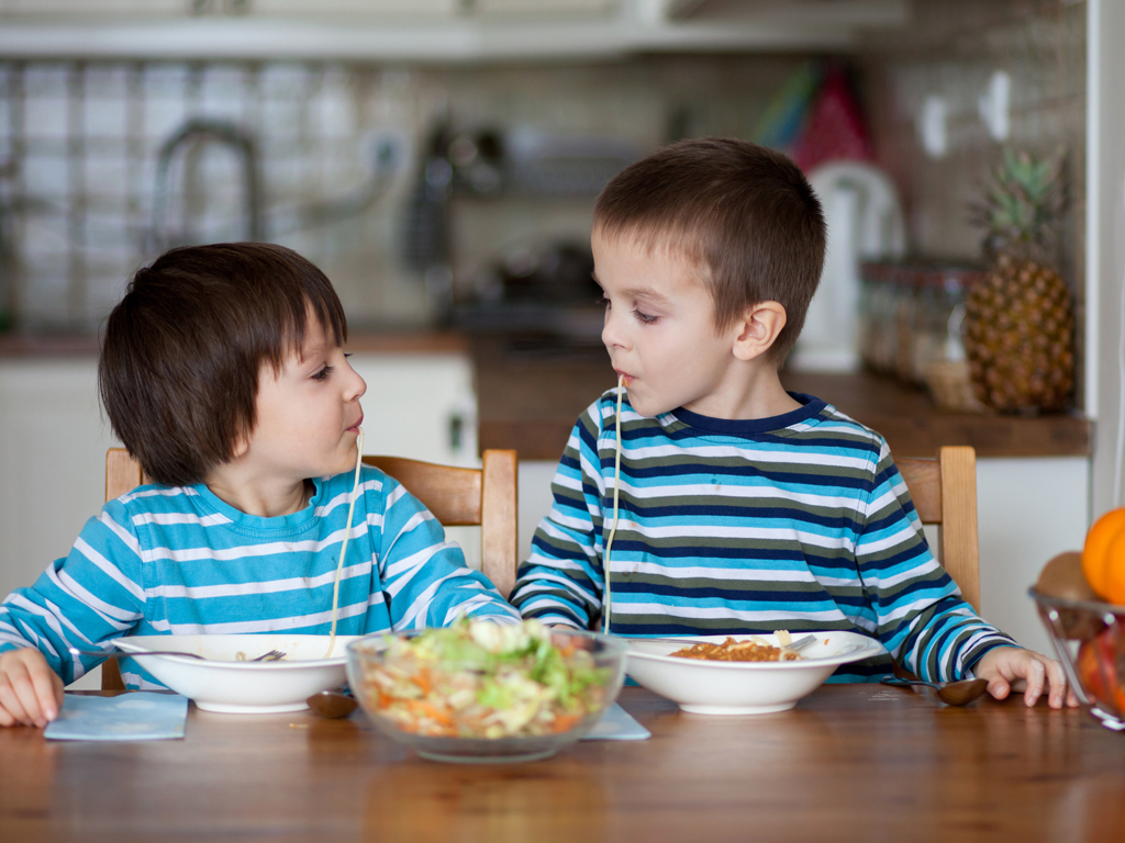Two sweet children, boy brothers, having for lunch spaghetti at home, enjoying tasty food