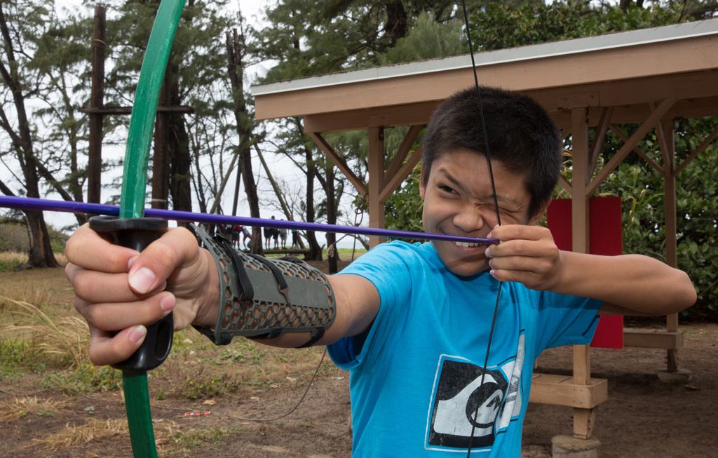 boy smiling while holding archery bow